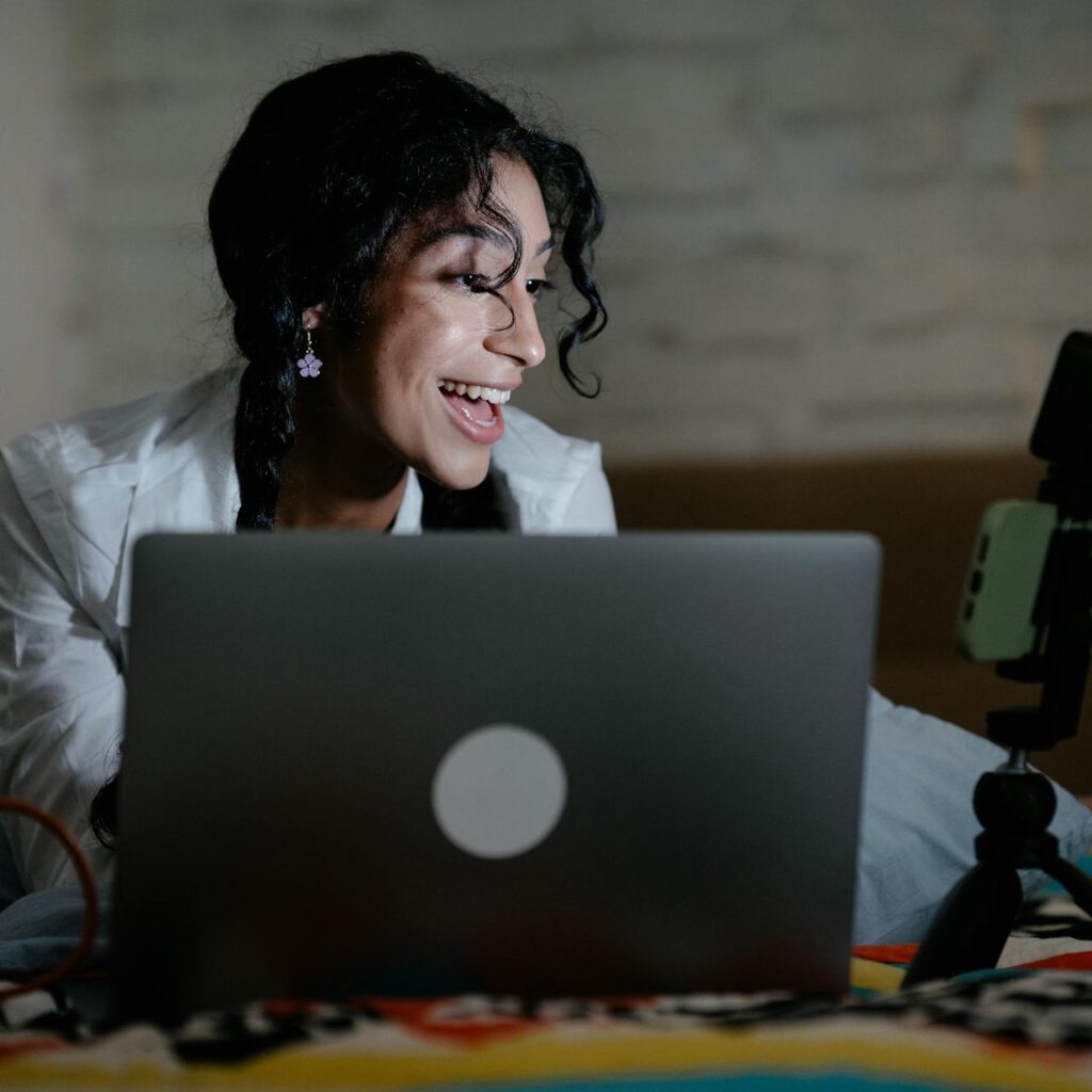 Lady streaming on a laptop while sitting on her bed.